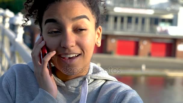 4k Videoclip von schönen gemischten Rassen afrikanisch-amerikanischen Mädchen Teenager junge Frau auf einer Brücke über einen Fluss, Kaffee trinken und auf einem Mobiltelefon sprechen — Stockvideo