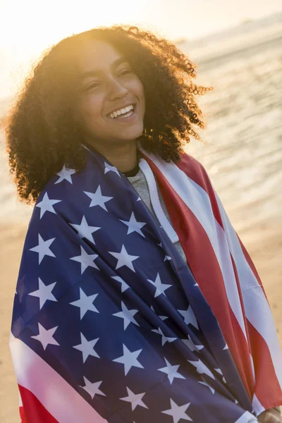 Misturado raça afro-americana menina adolescente envolto no EUA Bandeira na praia ao pôr do sol — Fotografia de Stock