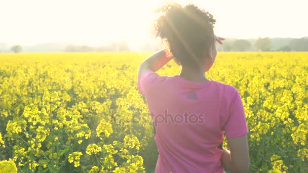 Женщина бегает или бегает трусцой и пьет бутылку воды в поле желтых цветов — стоковое видео