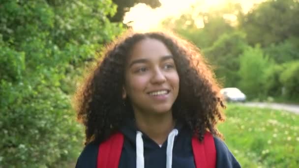 4 k video clip van mooie gelukkig gemengd ras African American girl tiener vrouwelijke jonge vrouw wandelen met rode rugzak op het platteland bij zonsondergang of zonsopgang — Stockvideo