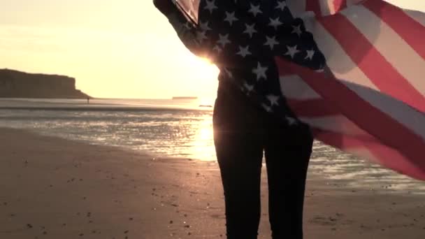 4K vídeo clipe de raça mista afro-americano menina adolescente mulher jovem envolto em um americano EUA Estrelas e listras bandeira em uma praia ao pôr do sol ou nascer do sol — Vídeo de Stock