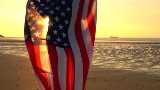 4k video clip van gemengd ras African American girl tiener vrouwelijke jonge vrouw gewikkeld in een American Stars en Stripes vlag op een strand bij zonsondergang of zonsopgang — Stockvideo