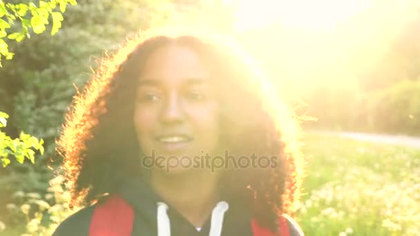 Piękny szczęśliwy mieszanej rasy African American dziewczyna nastolatek kobiece kobieta młoda kobieta pieszych z czerwony plecak na wsi na zachód lub wschód słońca — Wideo stockowe