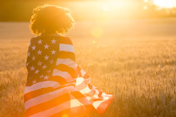 Meisje tiener verpakt in Usa vlag in veld bij zonsondergang — Stockfoto