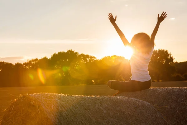 Jeune fille adolescente assise sur une balle de foin célébrant le coucher du soleil — Photo