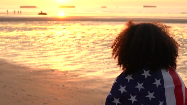 混合种族的视频剪辑非洲裔美国女孩少女女青年女子裹在美国星条旗旗 观看人们在沙滩上玩日落或日出 — 图库视频影像