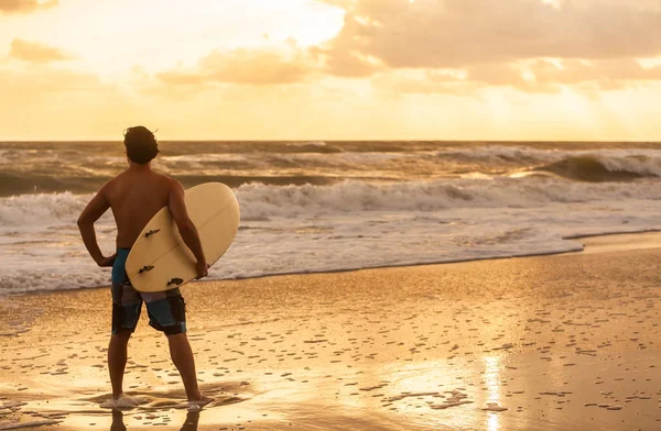 年轻男子男性冲浪者的后视图白色冲浪板在日落或日出海滩冲浪 — 图库照片