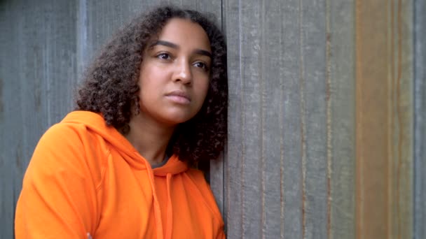 在城市环境中 漂亮的混血非洲裔美国少女身穿橙色帽衫 看上去悲伤或沉思 — 图库视频影像