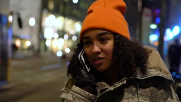 美丽的混合的种族女青年女孩穿着伪装夹克 一个橙色的帽子 晚上用手机聊天 在德国柏林亚历山大广场车站 — 图库视频影像