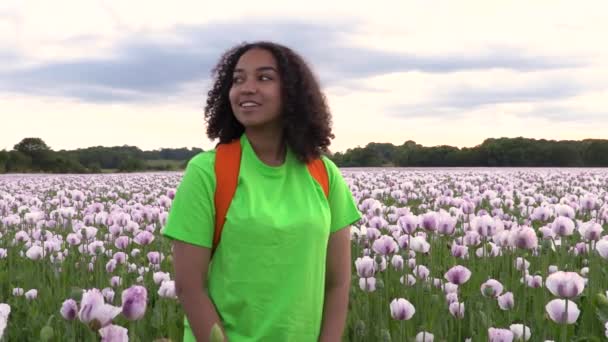 美しい幸せな混合レースアフリカ系アメリカ人の女の子の女の子の若い女性は ピンクのケシの花のフィールドを通ってパス上のオレンジ色のバックパックでハイキング — ストック動画