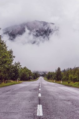Bulutların arkasında gizli dağlara giden asfalt yol. Bulutlar arasından çıkıntılı bir dağ.
