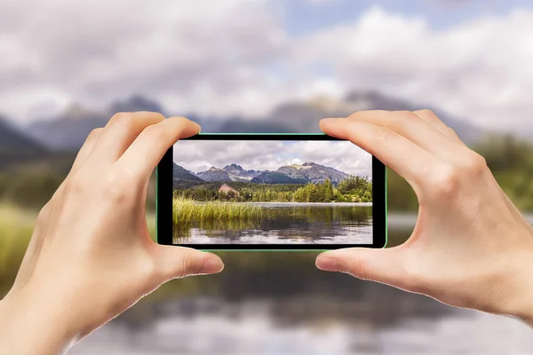 Bir cep telefonu holding eller. Dağ manzaraları bir smartphone kullanarak fotoğraf çekme.