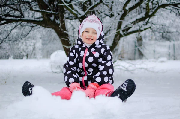 Una bambina seduta sulla neve nel parco invernale — Foto Stock