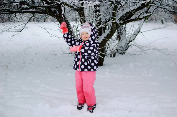 Una bambina seduta sulla neve nel parco invernale — Foto Stock