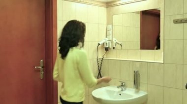 Sarı tişört ve siyah saçlı banyo lavabo, el yıkama ile genç bir kız portresi görünümü geri. Çekici kadın gülümseyerek, aynaya bakıyor