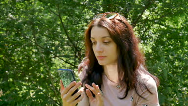 Yeşil ağaçlar zemin üzerine mavi Smartphone açık havada güzel esmer kadınla closeup portresi. Çekici kız cep telefonu ve Internet kullanarak tarama.