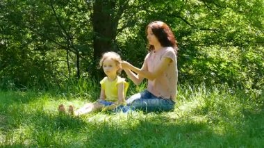 Onun küçük kızı saç modeli oturma parkta yeşil çimenlerin üzerinde yapıyor esmer anne portresi.