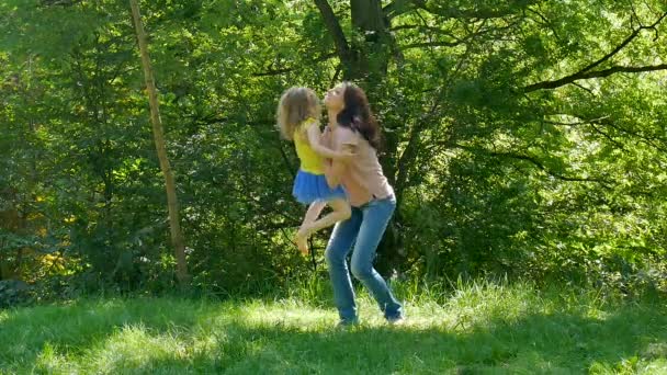 Glückliche Familie, die an einem sonnigen, warmen Tag die Zeit zusammen im Park verbringt. Brünette Mutter hebt ihre Tochter auf und wirbelt sie auf. kleines Mädchen küsst Mama. — Stockvideo