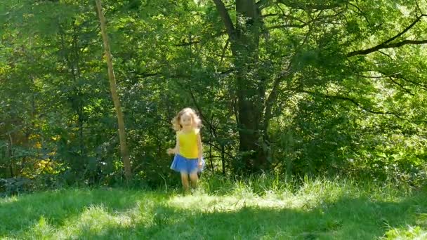La petite fille active court dans le parc jouant dehors sur l'herbe verte .