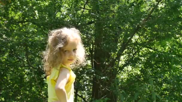 Närbild porträtt av lilla tjej med blont lockigt hår grimaserande och visar hennes tunga titta på kameran i parken under soliga sommardag. — Stockvideo