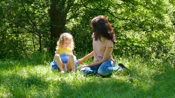 Glückliche junge brünette Mutter mit kleiner süßer Tochter mit blonden lockigen Haaren, die sich an sonnigen Sommertagen im Park ausruhen. — Stockvideo