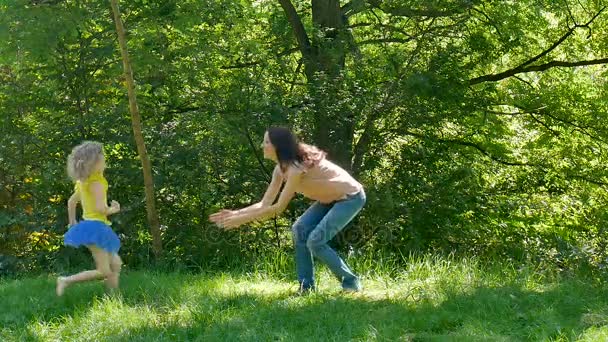 Ritratto di felice giovane madre in camicia rosa e jeans Raccogliere e roteare la sua piccola figlia sorridente nel parco durante la giornata calda soleggiata . — Video Stock