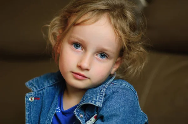 Retrato de uma menina encaracolada de olhos azuis com um olhar calmo. Ela está usando um colete de ganga — Fotografia de Stock