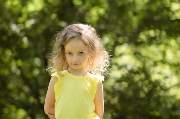 Closeup kuşkuyla, ironik olarak şüpheci, yarı-gülümseme, bir şüpheci küçük kız portresi. Yeşil ağaç arka planda portre — Stok fotoğraf