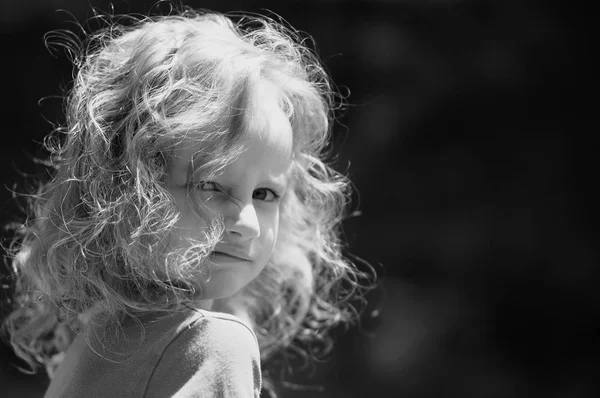 Retrato al aire libre de una linda niña con rizos oye, mirando hacia atrás sobre su hombro. blanco y negro — Foto de Stock