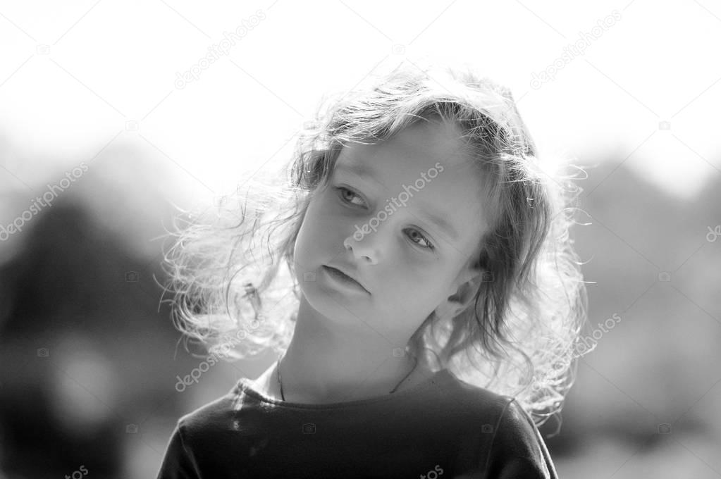 Black-and-white portrait of cute little girl , serious look, curly hair, sunny summer portrait