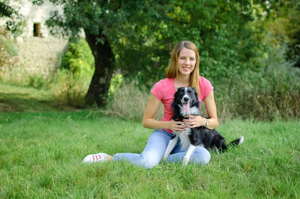 Retrato al aire libre de una mujer alegre con camisa rosa y pantalones vaqueros azules jugando con su perro blanco y negro en el parque durante el día de verano . — Foto de Stock