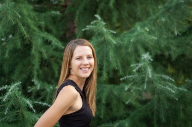 İnanılmaz gülümseyen kadın uzun Parlatıcı saç ayakta yakınındaki Ladin ağacı sırasında yaz saati ile siyah gömlekli.