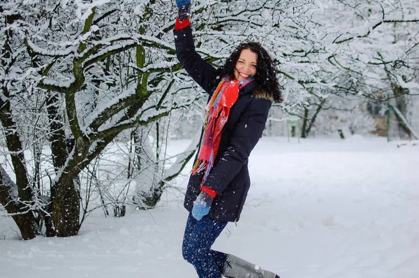 Aktiv lächelnde junge Brünette in rotem Schal, die während eines Tages draußen im verschneiten Park Winterspiele spielt. — Stockfoto