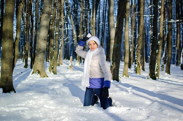 Приваблива молода жінка є із задоволенням у Snowy парк під час за сонячної погоди взимку. Дівчина є ігрового в боротьбі сніжок і дивлячись на камеру. — стокове фото