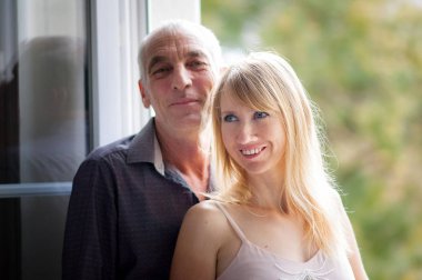 Ateşli ve Seksi Orta yaşlı Kadın Yaşlı Kocasının Sevinen Kucaklaşması Evlerinin İçindeki Açık Pencere 'nin yanında duruyordu. Yaş farkı olan çift.