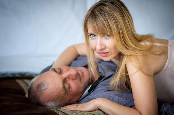 Hermosa mujer rubia en lencería sexy abrazando a su marido mayor acostado en la cama. Pareja con diferencia de edad . —  Fotos de Stock
