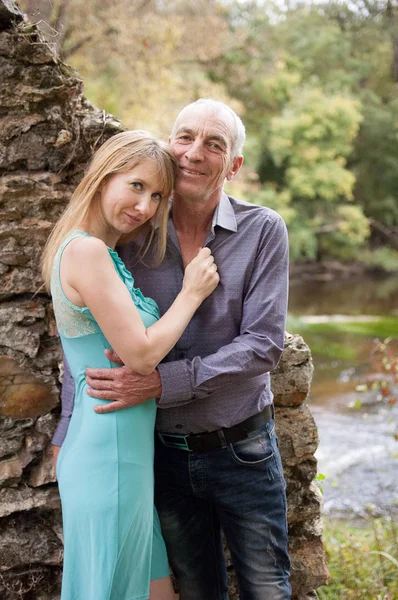 Retrato al aire libre de pareja feliz con diferencia de edad Abrazarse mutuamente de pie en el parque durante el soleado y cálido día de verano . — Foto de Stock