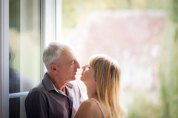 Привлекательная блондинка обнимает симпатичного пожилого мужчину и смотрит на него с любовью и страстью в глазах. Пара с разницей в возрасте . — стоковое фото