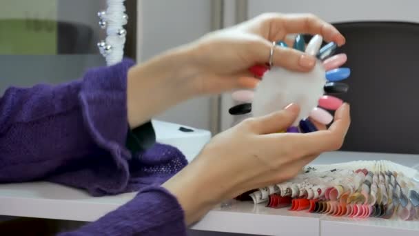 Βίντεο closeup της πηκτής καρφιά παλέτα πίνακα χρωμάτων στο σαλόνι ομορφιάς. Γυναικεία χέρια επιλέγοντας υπεριώδους βερνίκι νυχιών. — Αρχείο Βίντεο