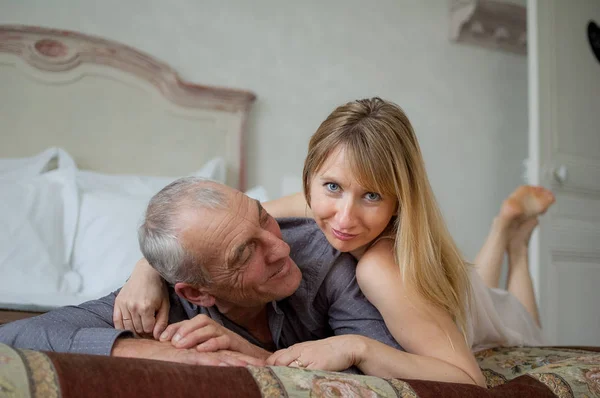 Retrato interior de pareja alegre con diferencia de edad acostada en la cama . —  Fotos de Stock
