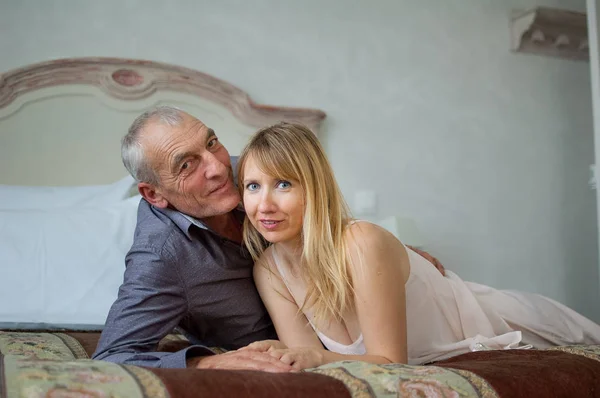 Retrato de pareja sonriente con diferencia de edad. Hermosa joven con su amante mayor acostada en la cama. Hombre besando a su novia . — Foto de Stock