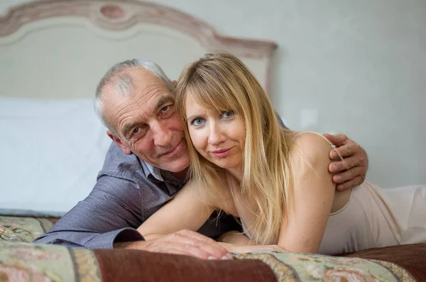 Neşeli çift yatakta yatıyordu yaş farkı ile portresi. Adam kız arkadaşı sarılma. — Stok fotoğraf