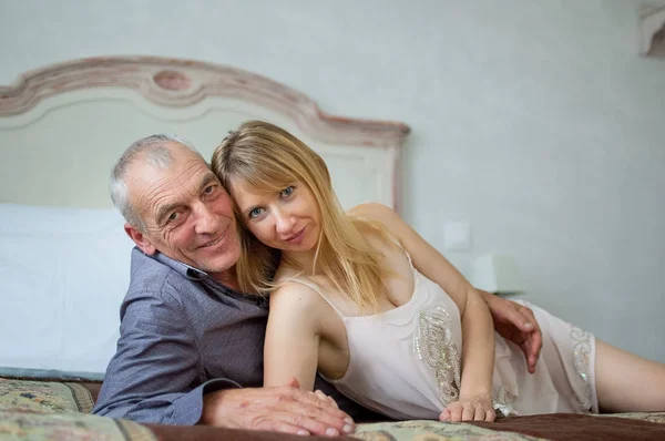 Retrato de feliz pareja encantadora con diferencia de edad. Hermosa joven rubia con su amante mayor acostada en la cama . —  Fotos de Stock