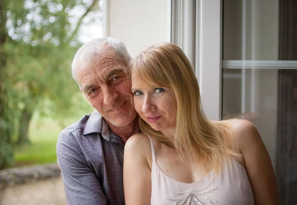 Primer plano Retrato de pareja feliz con diferencia de edad Abrazándose cerca de la ventana en su casa durante el día caluroso de verano. Concepto de Psicología de Relaciones . — Foto de Stock