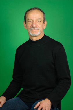 Yeşil bir arka plan üzerinde olgun bir adam portresi. Siyah kazak, hayırsever yüz ifadesi, gri saçlı, iyi kesilmiş sakal