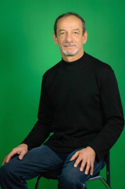 Siyah kazak ve karanlık kot Studio yeşil bir arka koltukta oturan iyi kesilmiş sakallı yakışıklı gri saçlı olgun adam