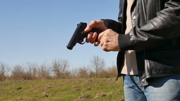 Manos masculinas sosteniendo el arma con balas en el fondo azul durante el soleado día de primavera al aire libre. Concepto de uso de armas — Vídeos de Stock