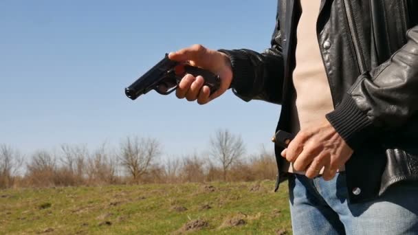 屋外の晴れた春の日に青い空を背景に弾丸と銃を保持している年配の男性の手。武器使用コンセプト — ストック動画