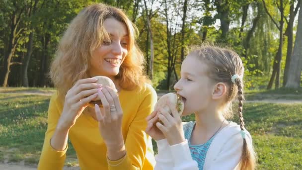 Giovane madre e piccola figlia sta cenando pasto fast food trascorrere del tempo nel parco durante il fine settimana in famiglia. Stile di vita malsano, concetti di pranzo — Video Stock