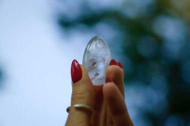 Vumfit, imbuilding veya meditasyon için şeffaf ametist kuvars yoni yumurta ile Kadın el. Gökyüzü ve gündoğumu arka plan açık havada ellerde parlayan kristal yumurta. Kadın sağlığı kavramı.